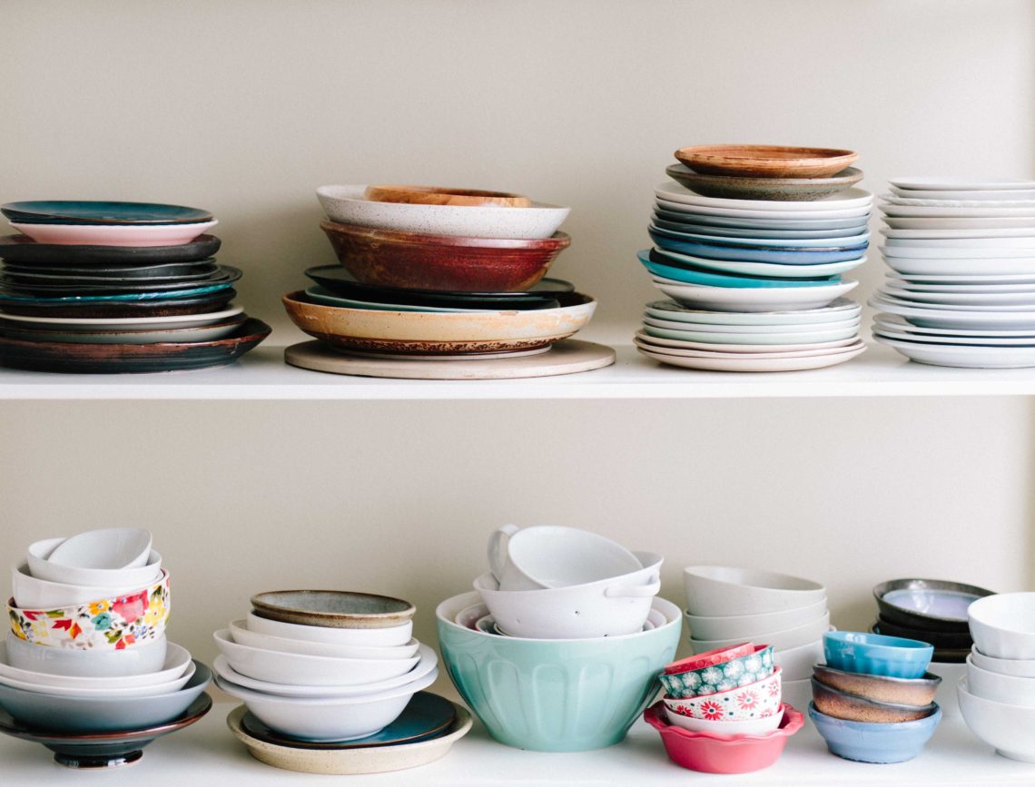 Various bowls and plates in different colours on a shelf.