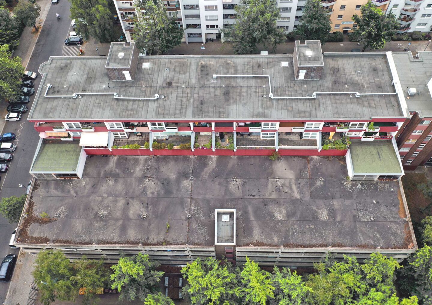 Luftaufnahme eines Wohnviertels mit mehrstöckigen Wohngebäuden und begrünten Innenhöfen. Autos sind entlang der Straßen geparkt, und viele Bäume säumen die Gehwege sowie die Höfe